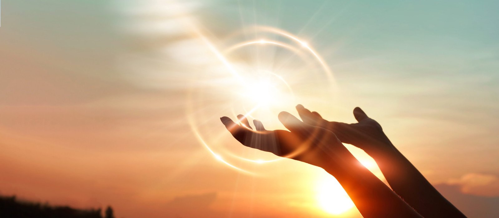 Two silhouetted hands reach upward toward a glowing light with circular lens flare against an orange and blue sunset sky above a dark horizon.