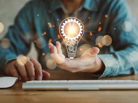 A hand held open beneath an illuminated light-bulb graphic above a keyboard.